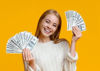 Young investor. Happy millennial girl holding lots of dollars on orange background with free space